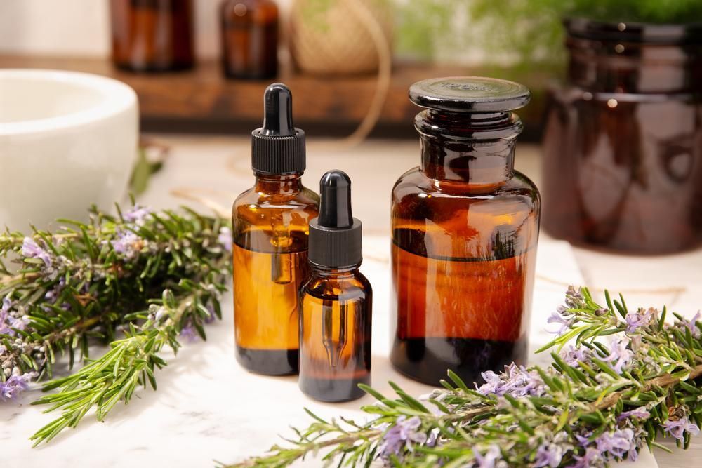 A Table Topped With Bottles Of Essential Oil And Rosemary Flowers — Mackay Skin Clinic In North Mackay, QLD