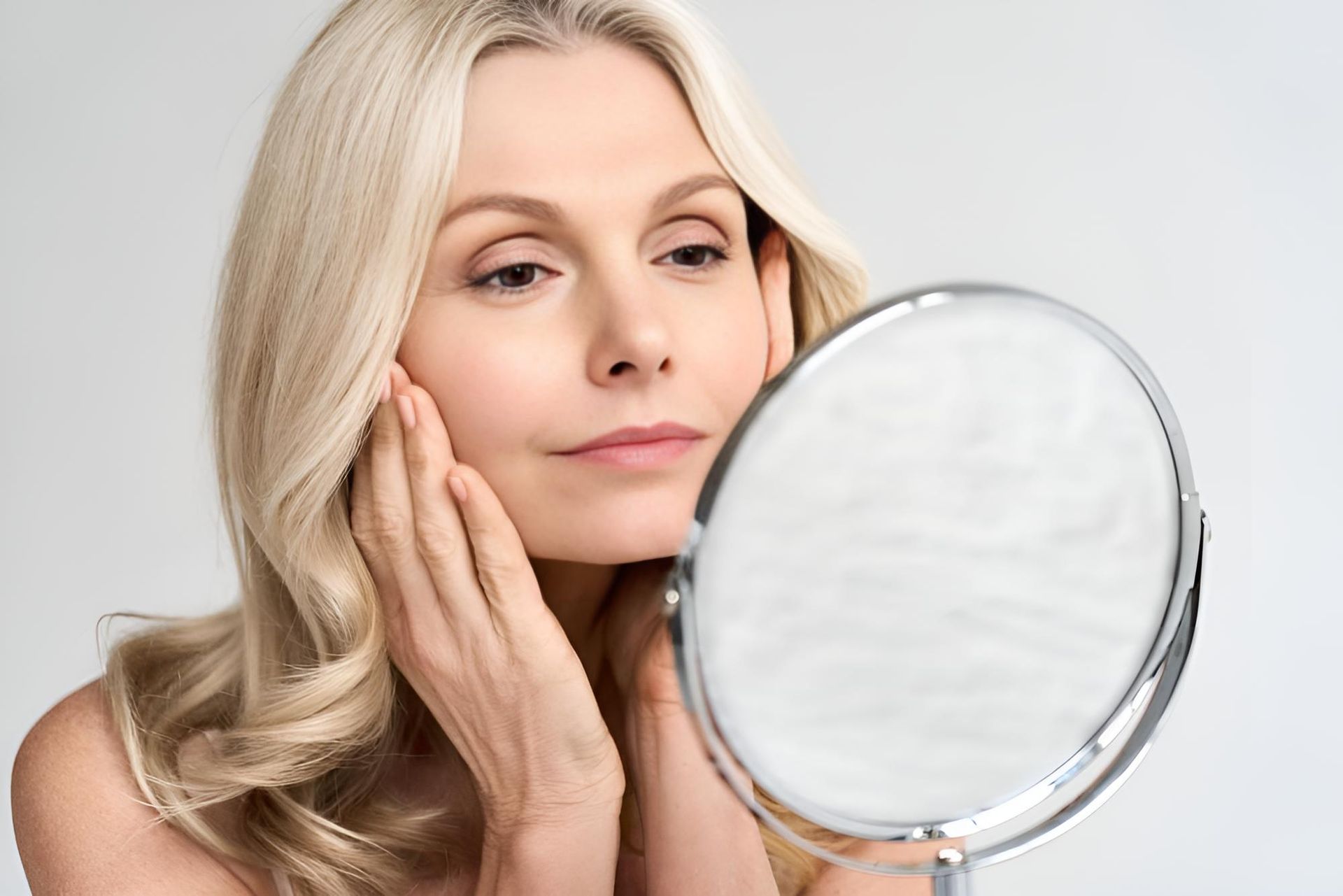 A Woman Is Looking At Her Face In A Mirror — Mackay Skin Clinic In Proserpine, QLD