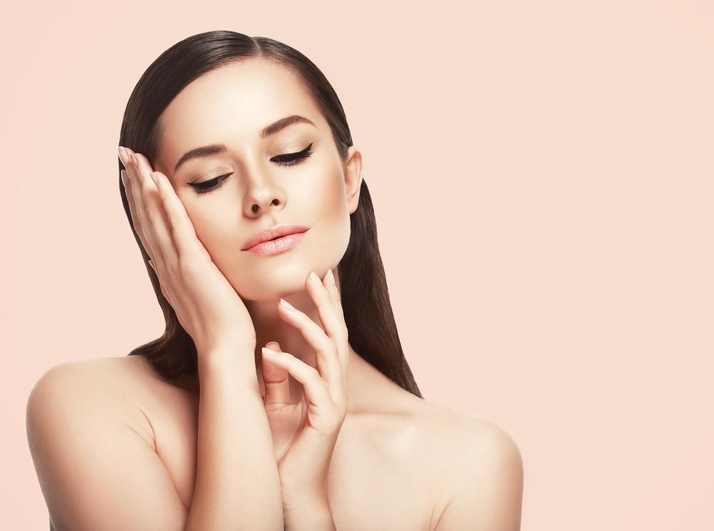 A Woman Is Touching Her Face With Her Hands And Smiling — Mackay Skin Clinic In North Mackay, QLD