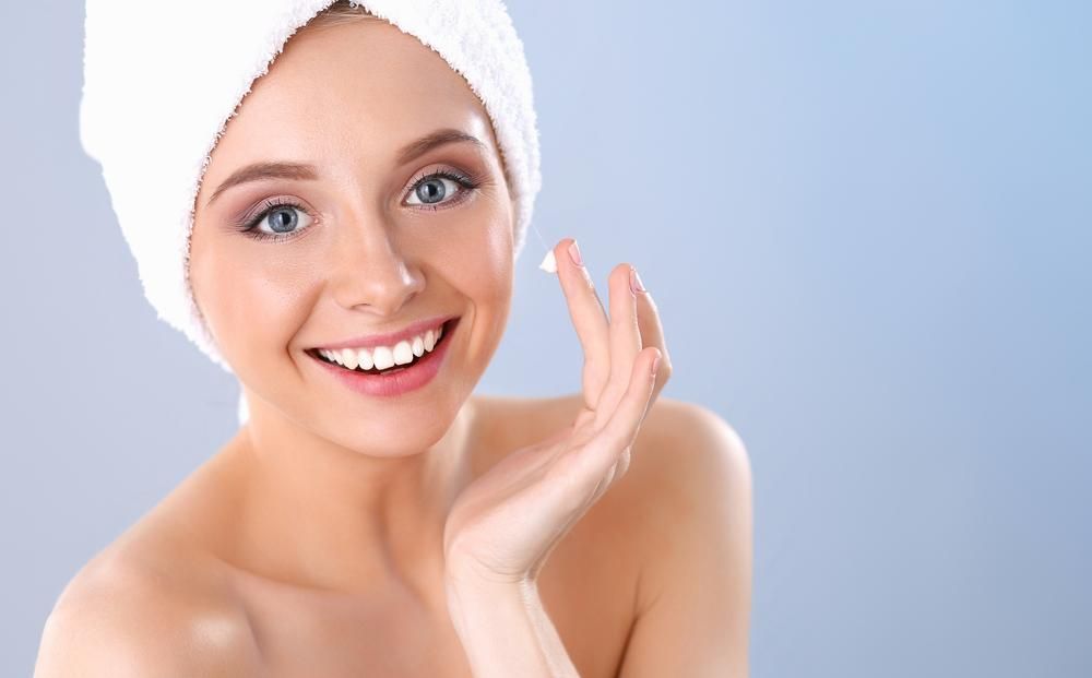 A Woman Smiling And Applying Cream To Her Face — Mackay Skin Clinic In North Mackay, QLD