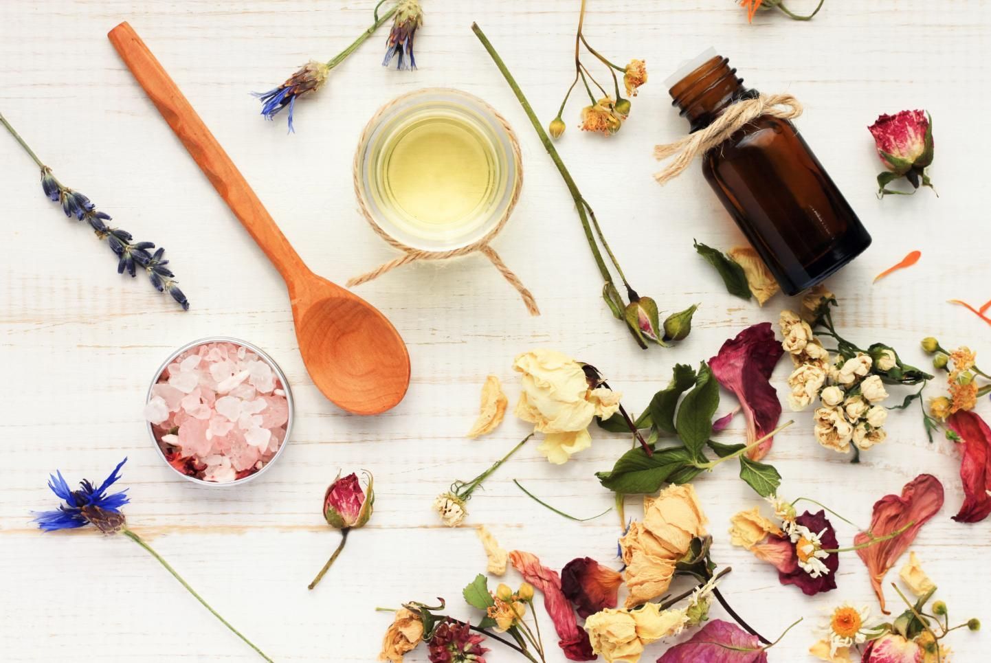 A Bottle Of Essential Oil Surrounded By Dried Flowers And A Wooden Spoon — Mackay Skin Clinic In North Mackay, QLD