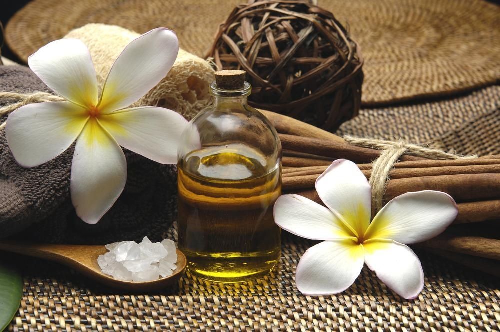 A Bottle Of Oil Next To A Spoon Of Salt And Flowers — Mackay Skin Clinic In North Mackay, QLD