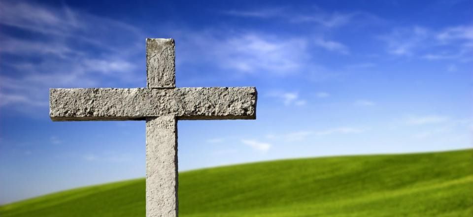 Stone cross on a green hill under a blue sky with clouds