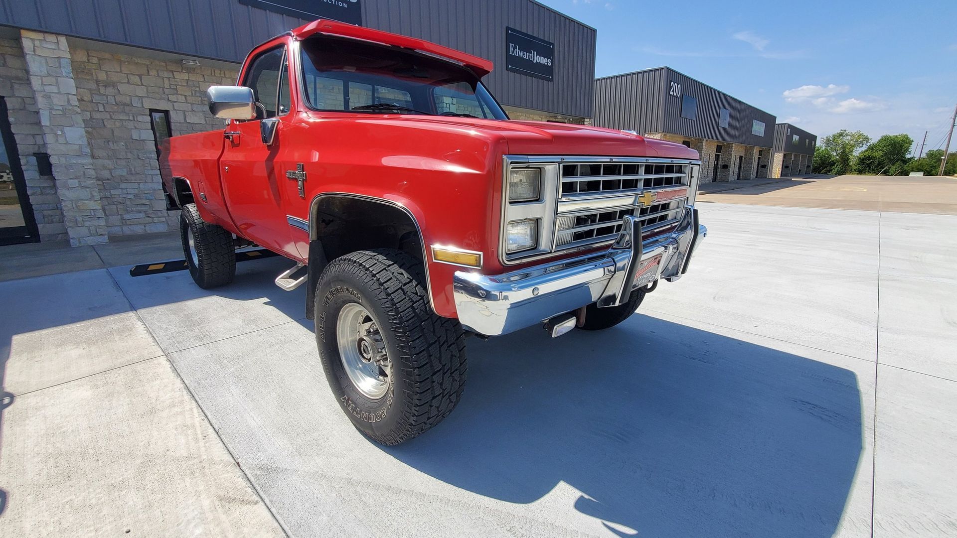 A red truck is parked in a parking lot in front of a building.