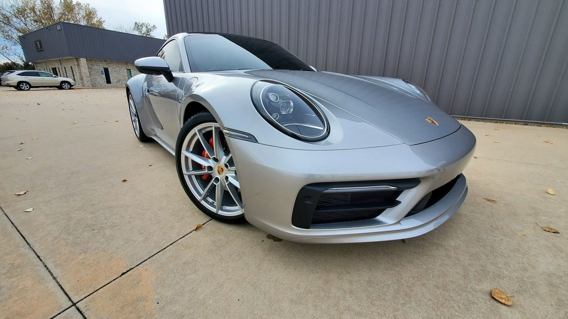 A silver porsche 911 is parked in a driveway in front of a building.