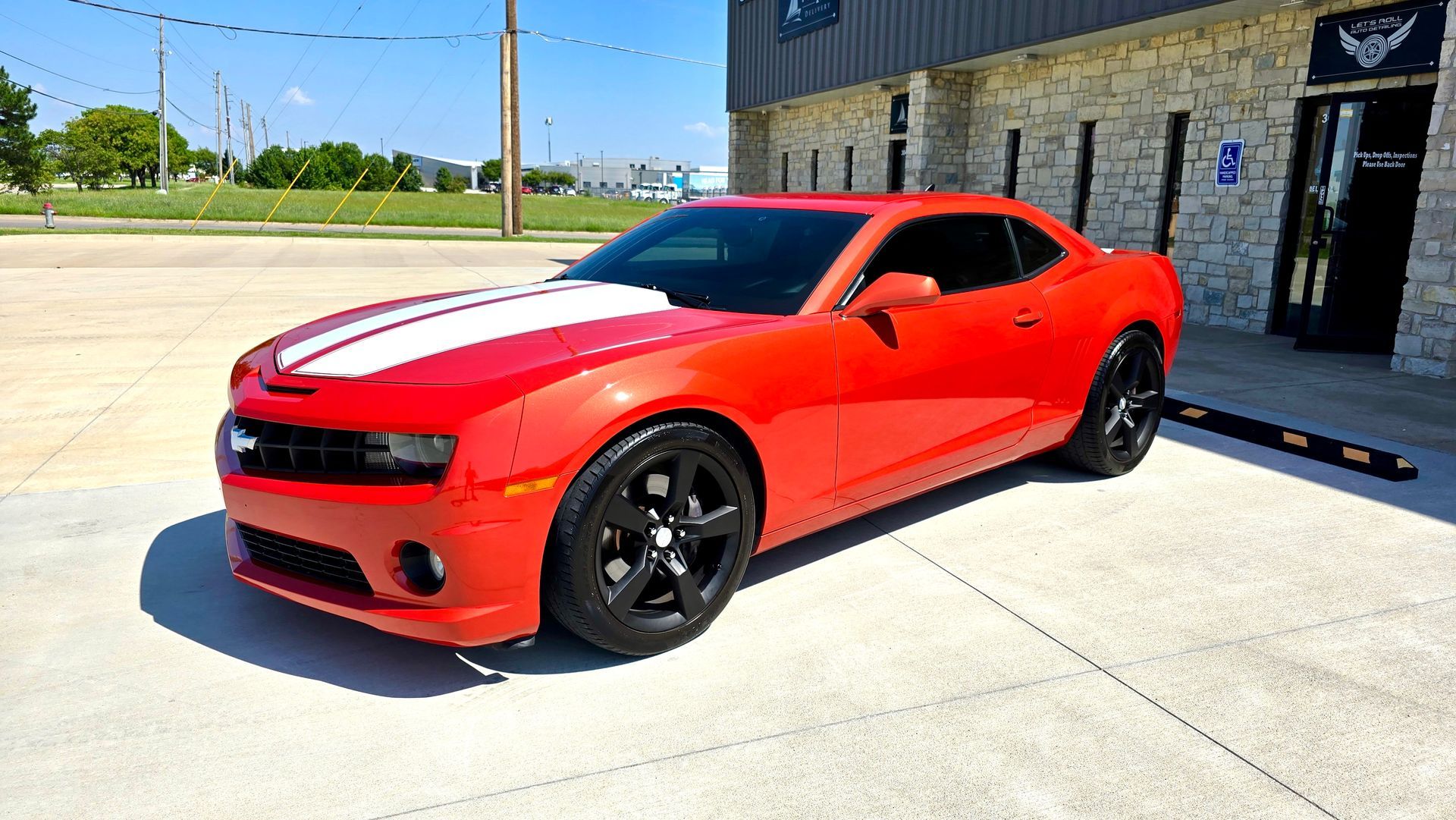 Red Camaro with white racing stripes, black rims, parked in front of a building.