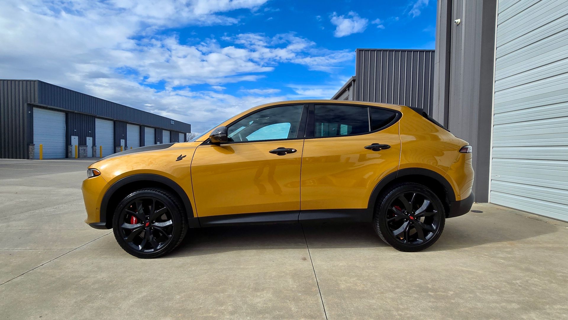 Yellow SUV parked next to a gray building, black wheels, blue sky background.