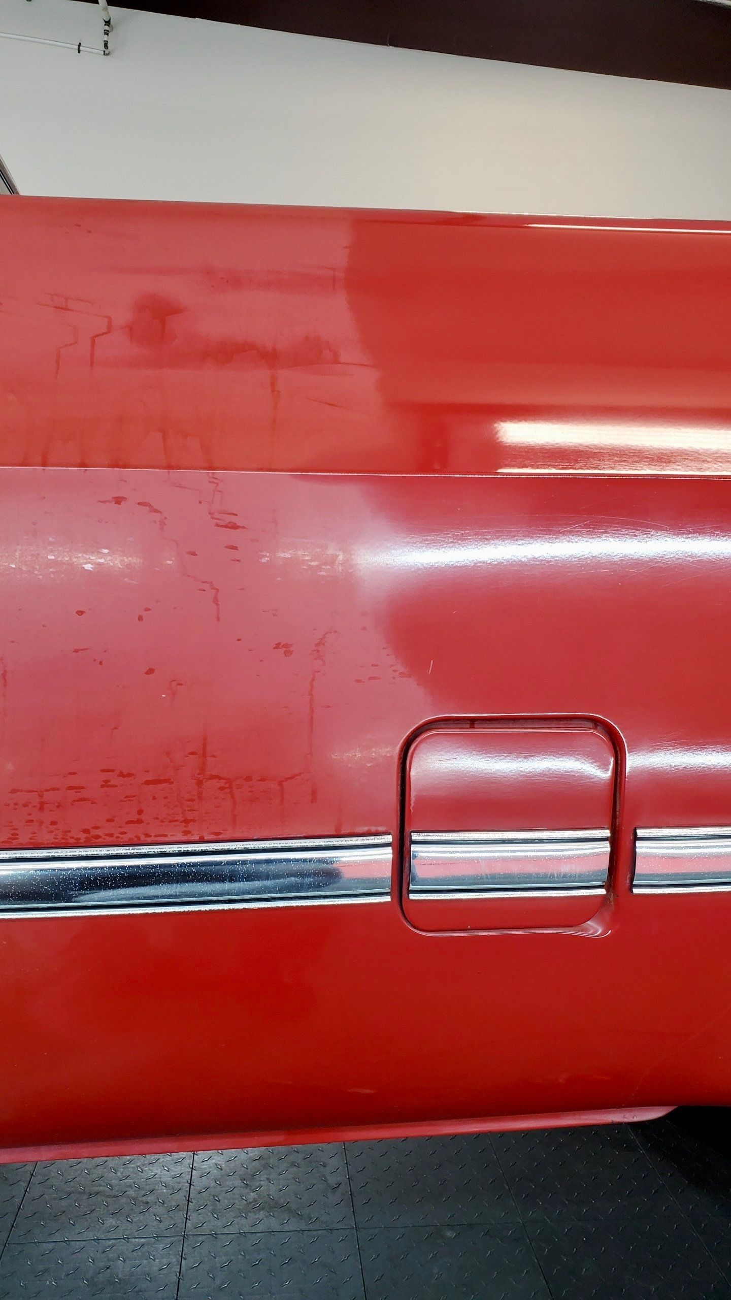 A red car with a chrome trim is parked in a garage.