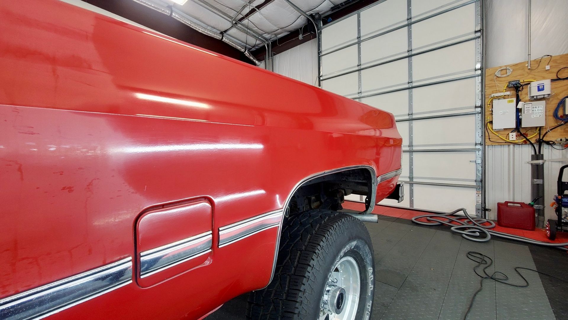 A red truck is parked in a garage next to a garage door.