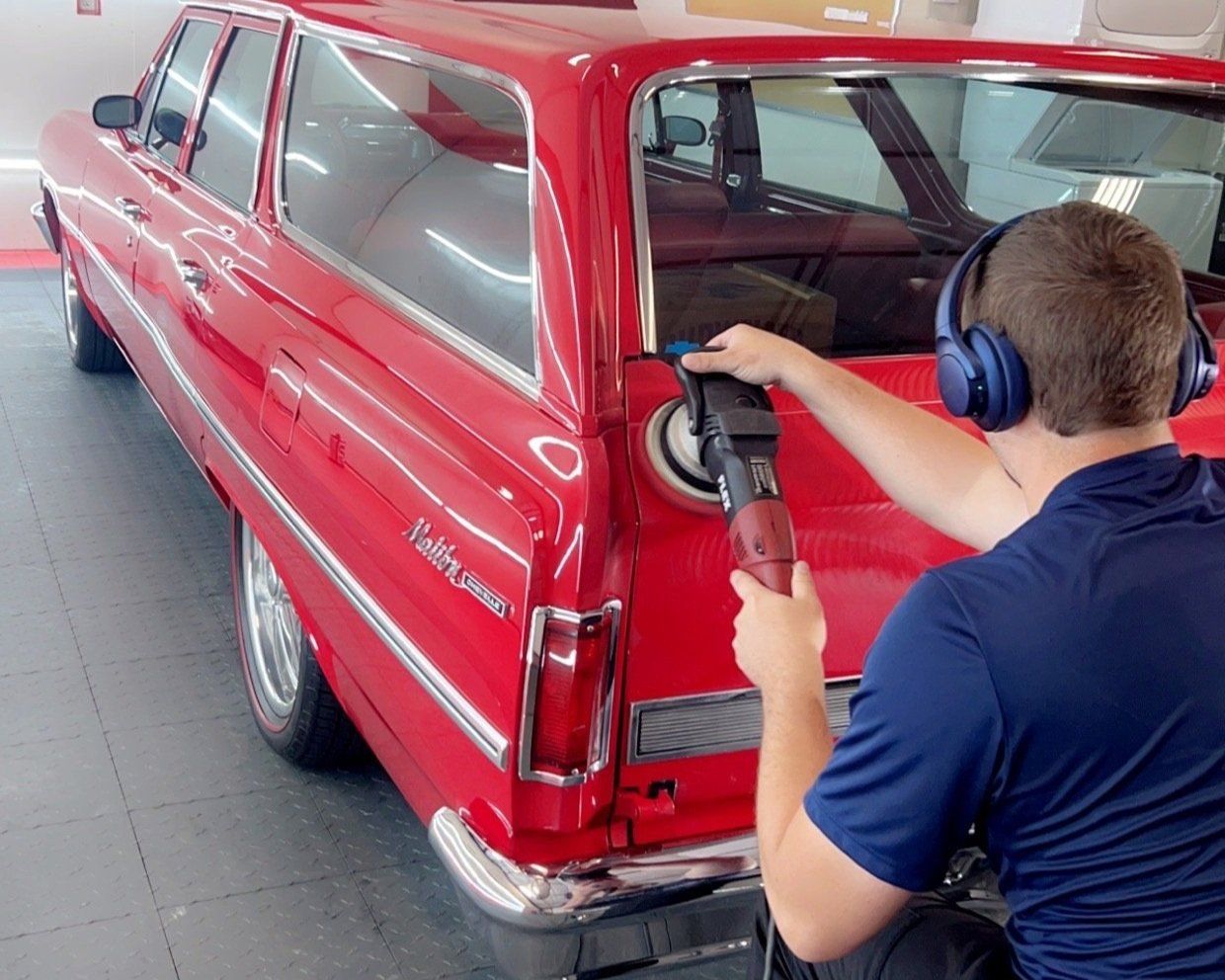 A man wearing headphones is polishing a red car