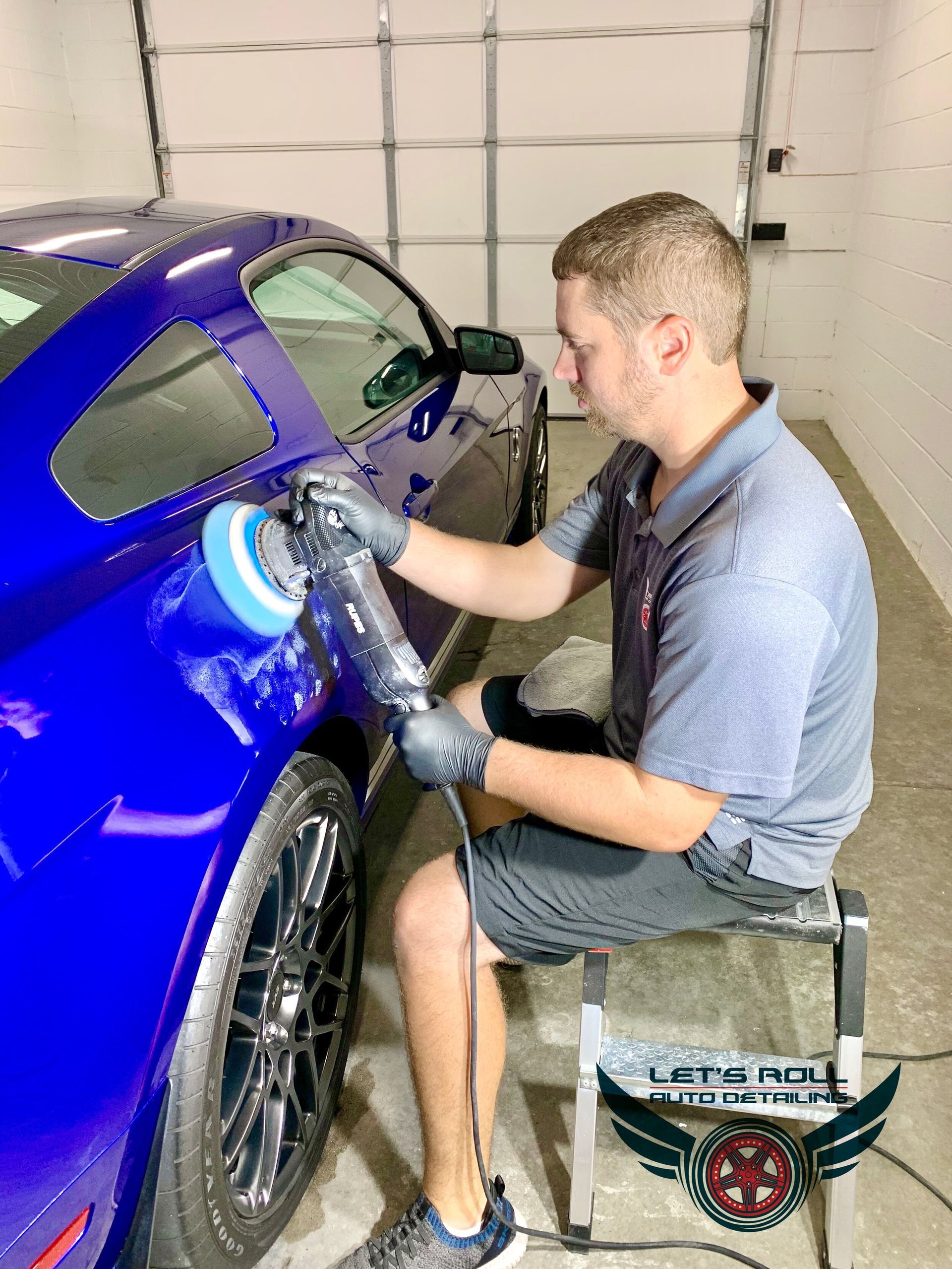 A man is polishing a blue car in a garage.