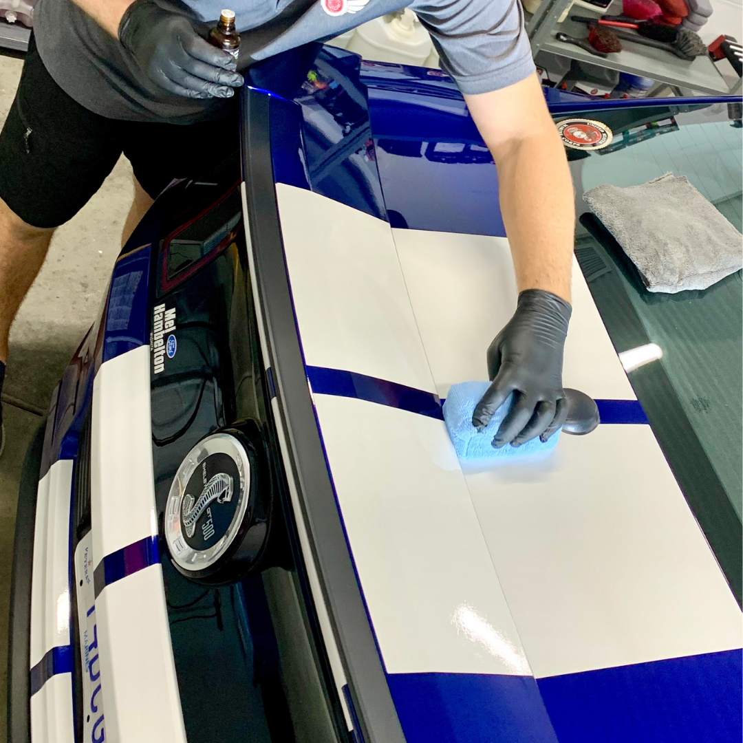 A man is cleaning the hood of a car with a sponge