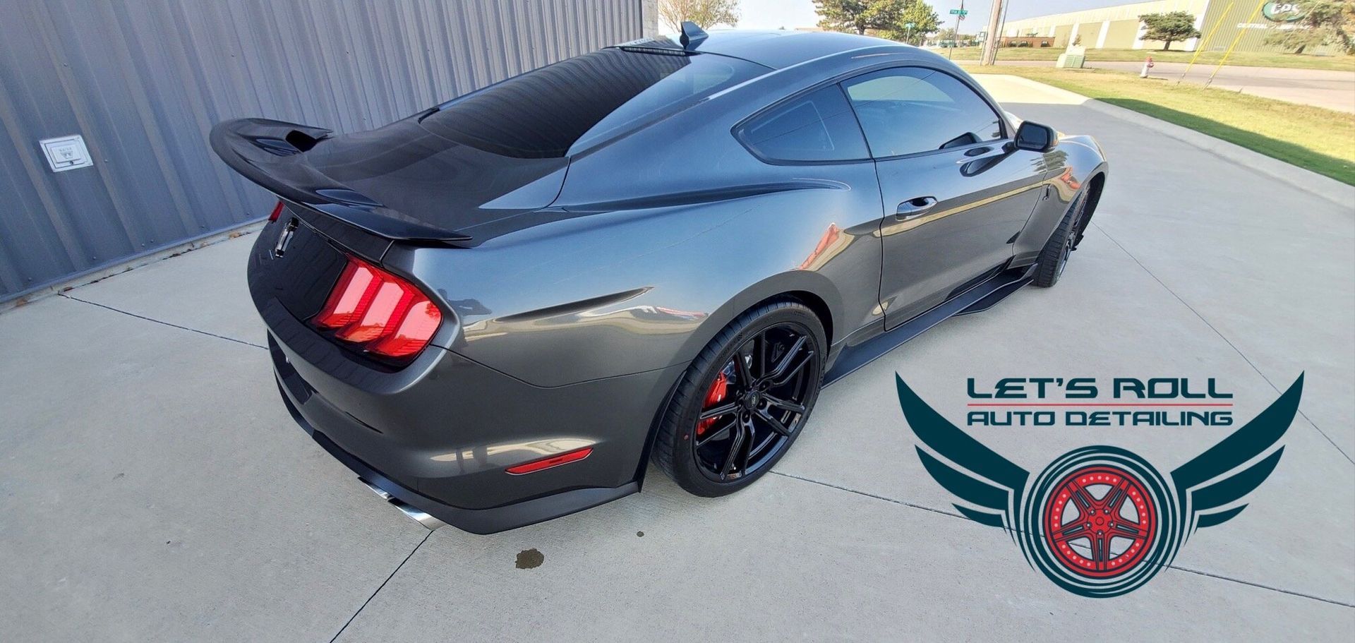 A black mustang is parked in a driveway next to a building.