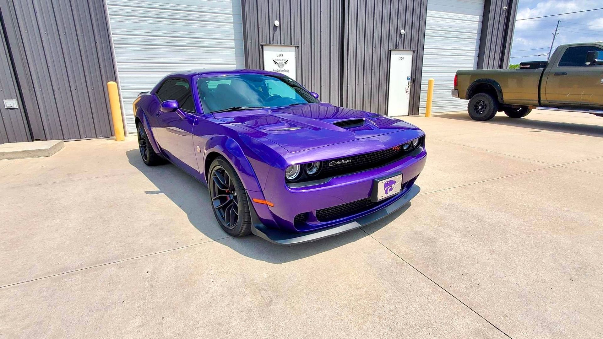 A purple dodge challenger is parked in front of a building.