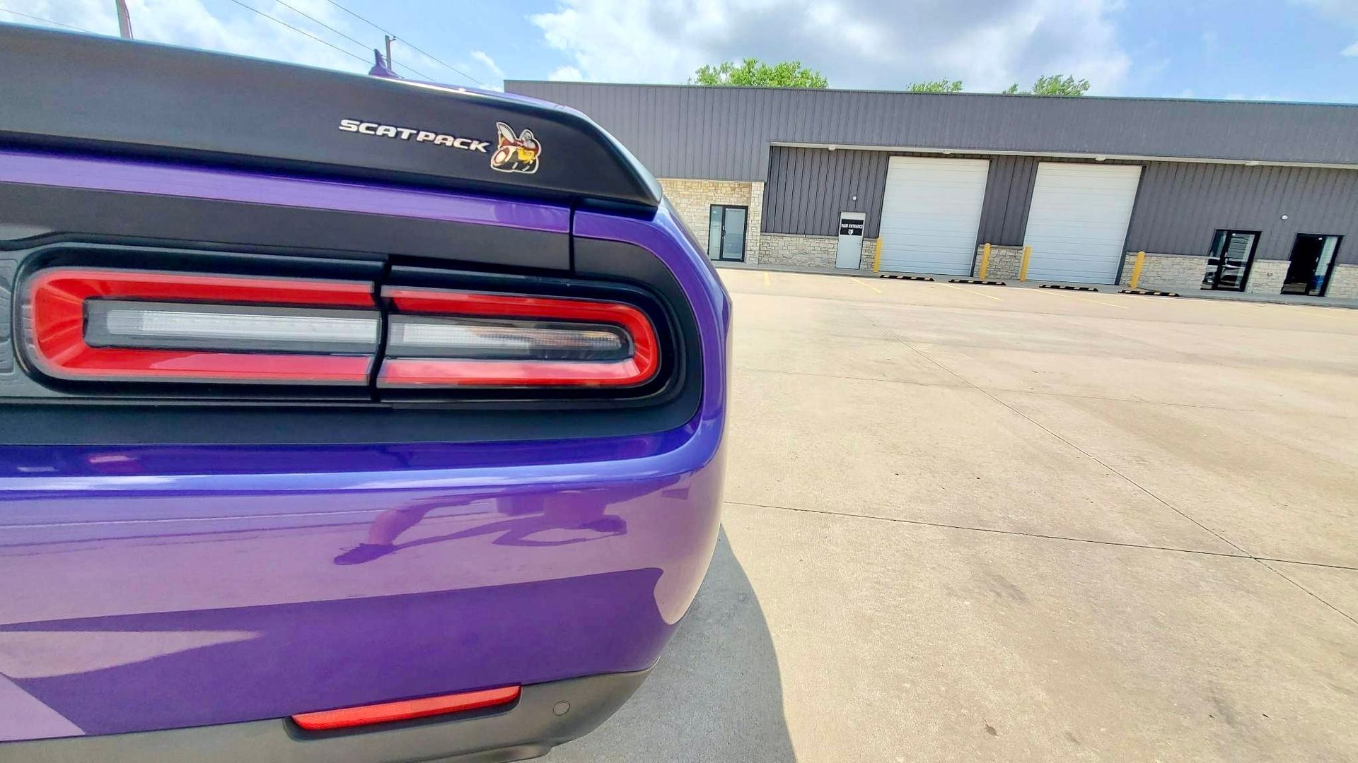 A purple dodge challenger is parked in a parking lot in front of a building.