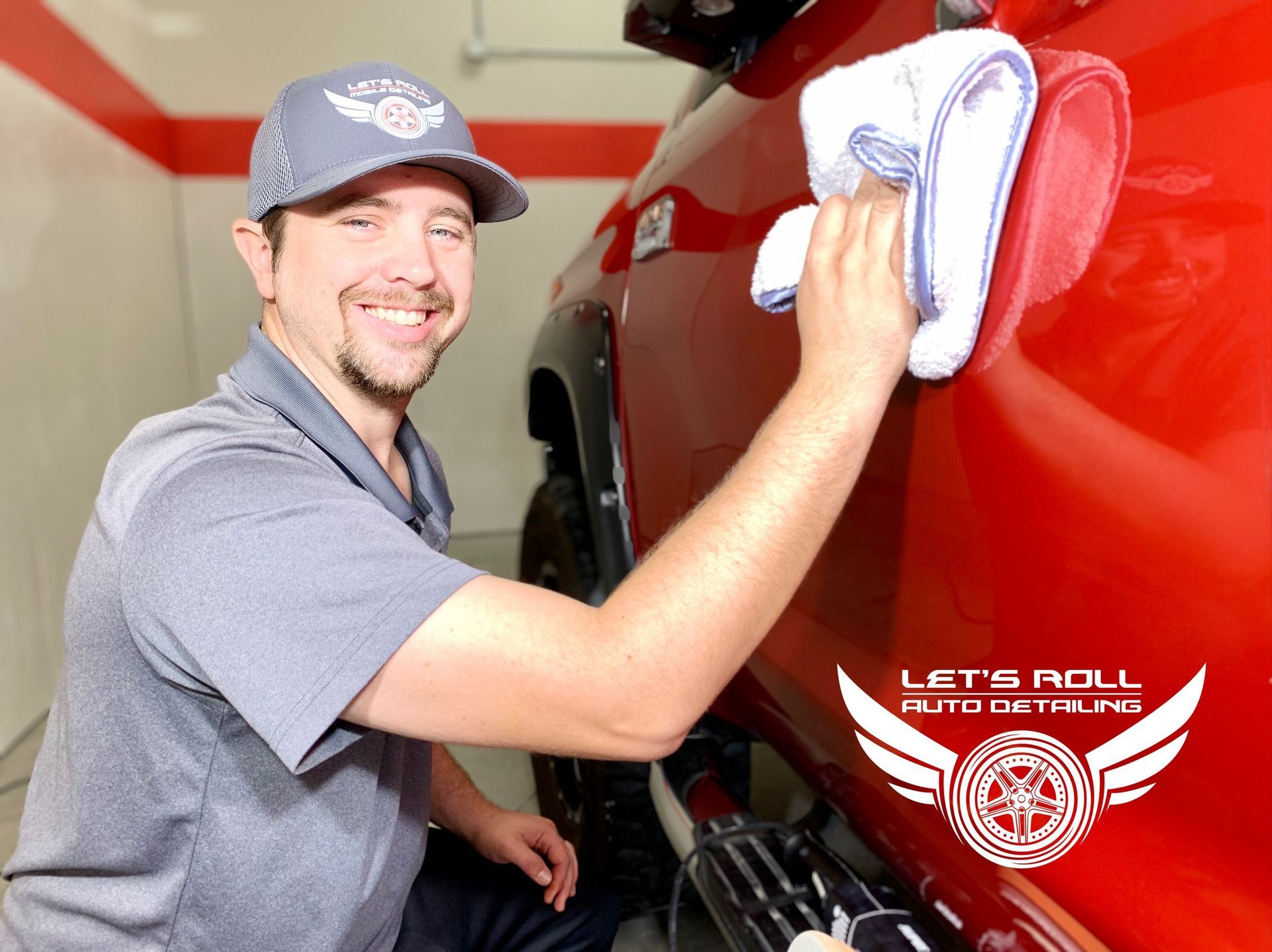 A man is polishing a red truck with a towel.