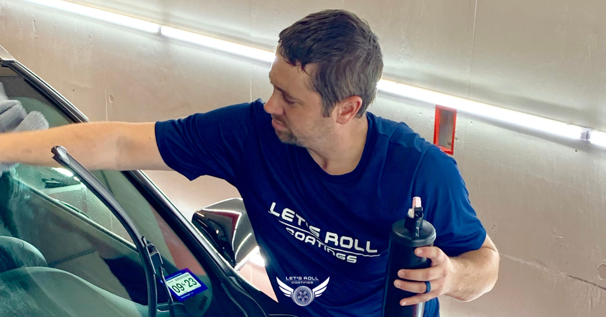 A man in a blue shirt is cleaning the windshield of a car.