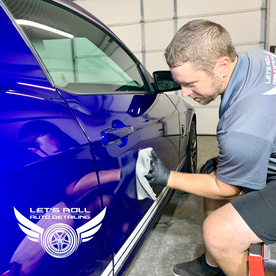 A man is cleaning a blue car with a cloth