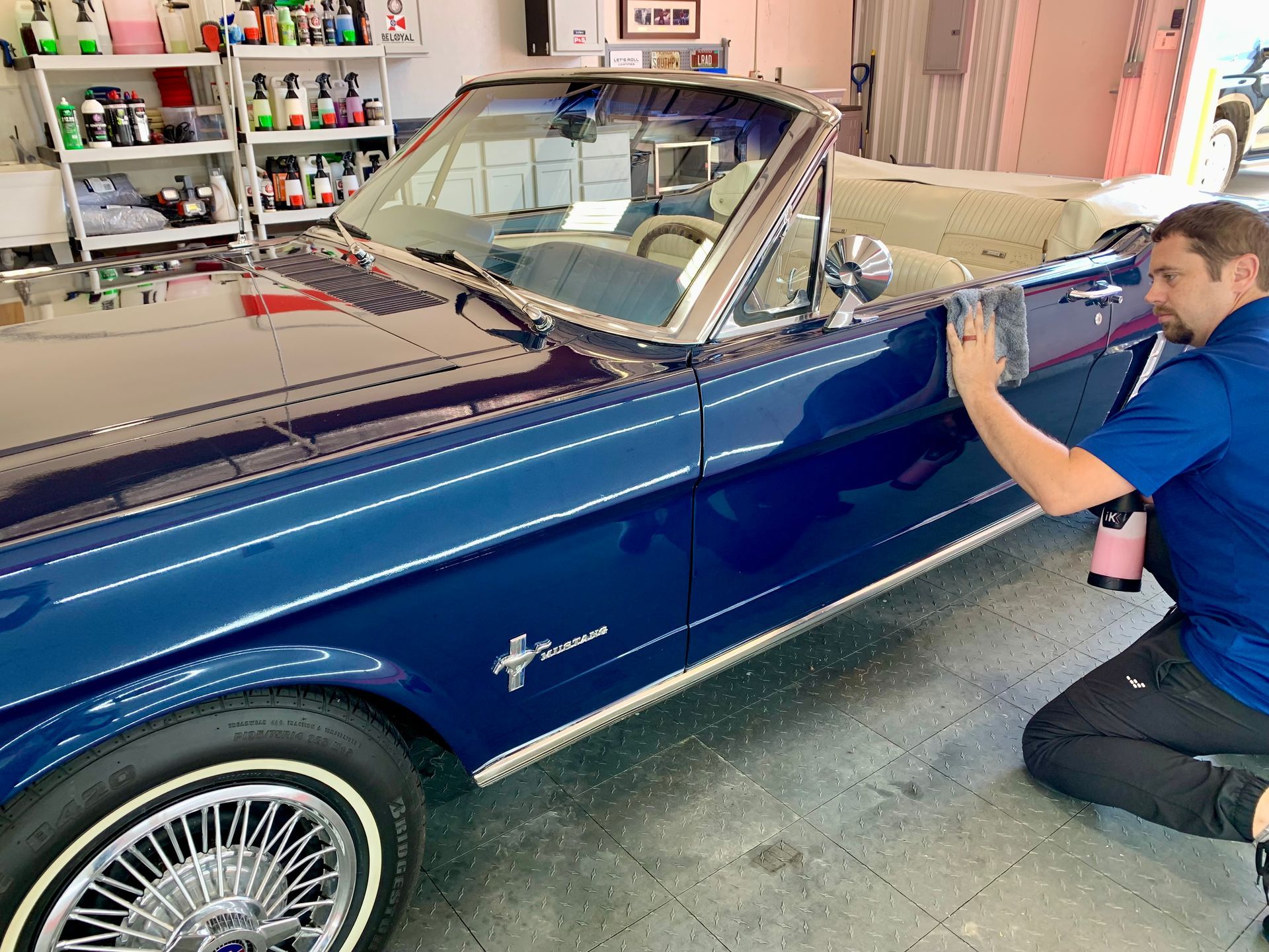 A man is kneeling down next to a blue car in a garage.