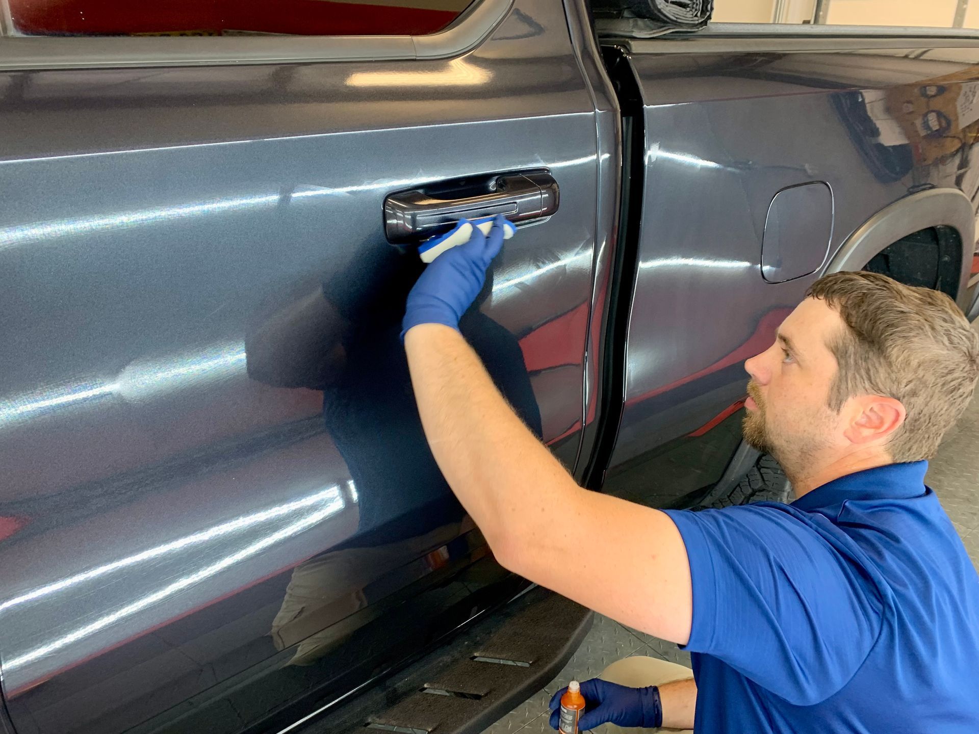 A man in a blue shirt is working on the door handle of a truck.