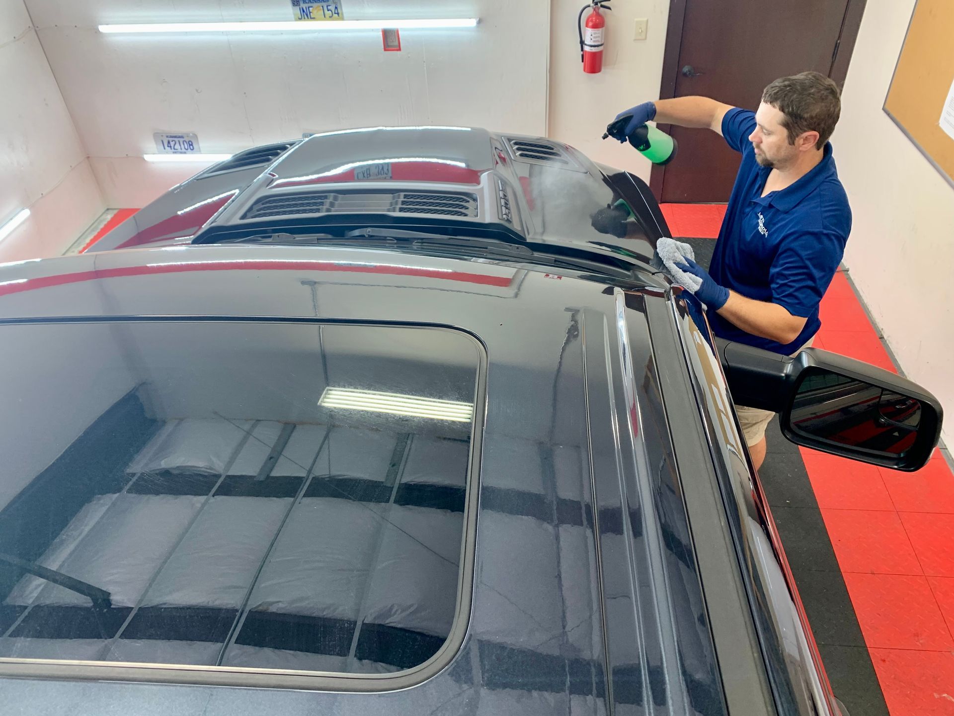 A man is cleaning the roof of a car in a garage.