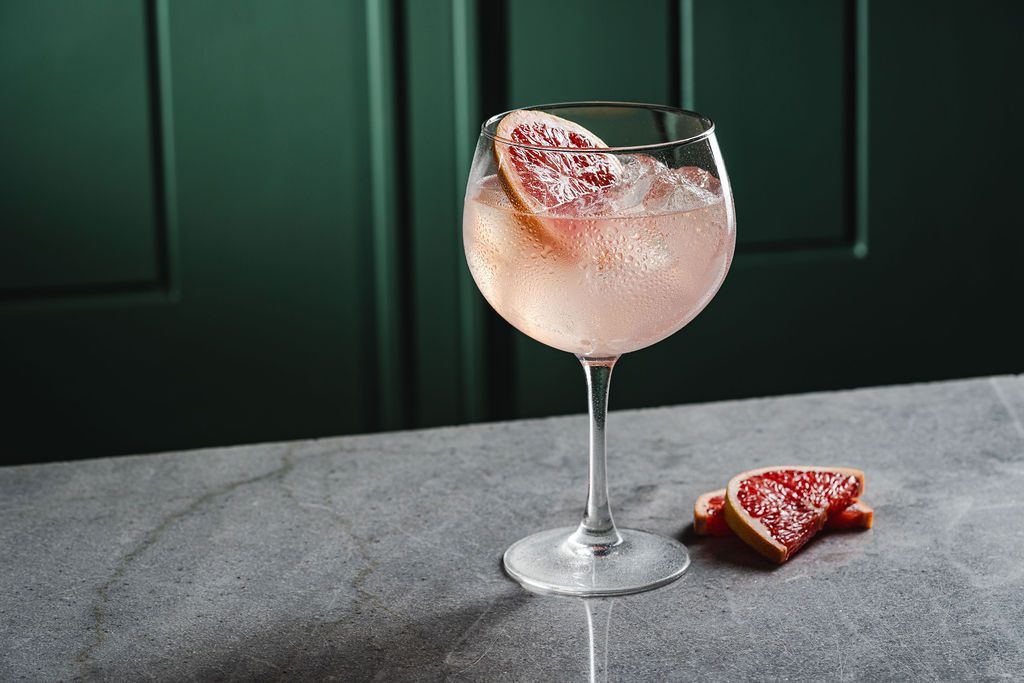 Three layered cocktails on a black table, topped with citrus slices and ice.
