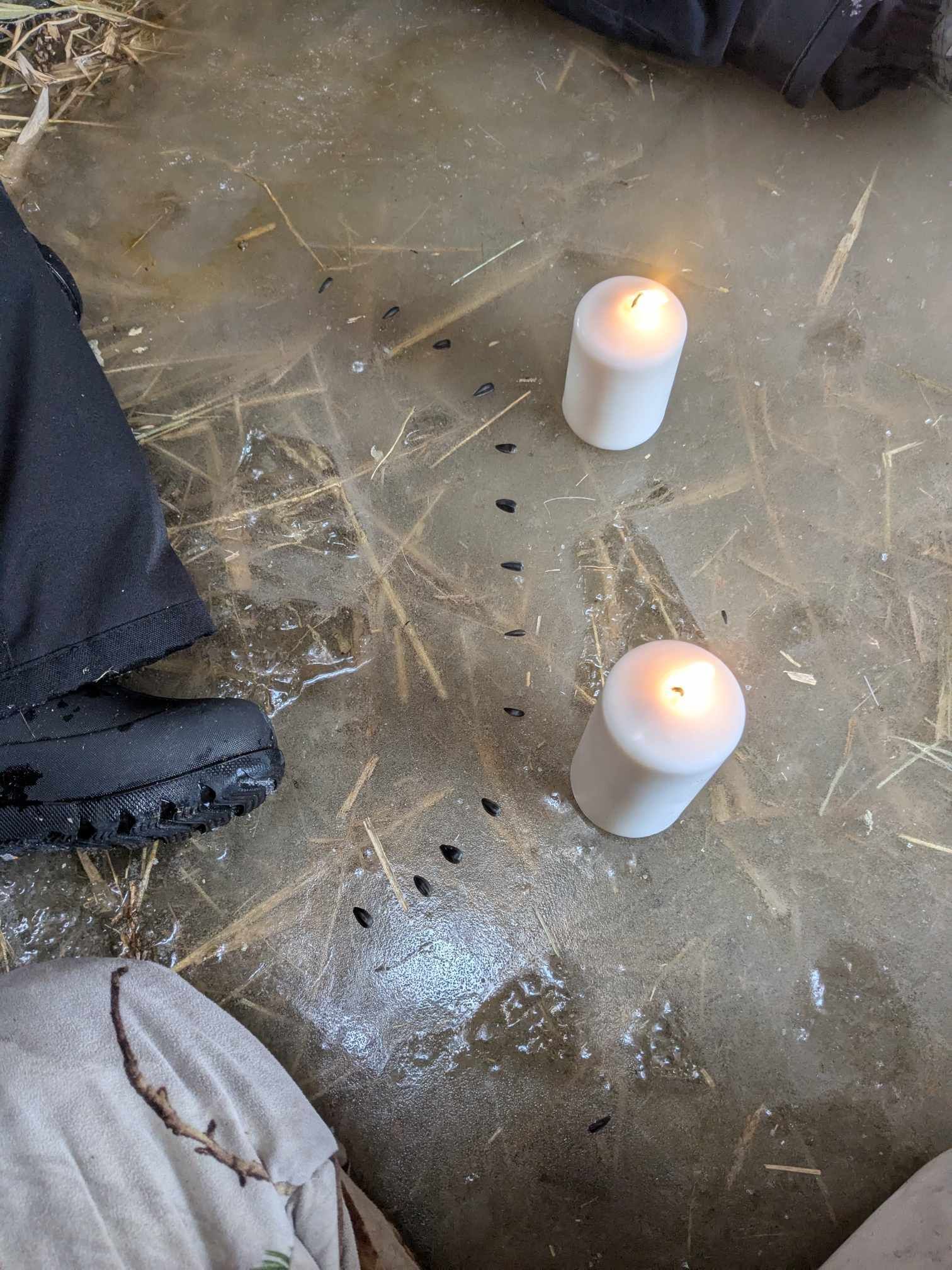 Two candles are sitting on the floor next to a person 's foot.