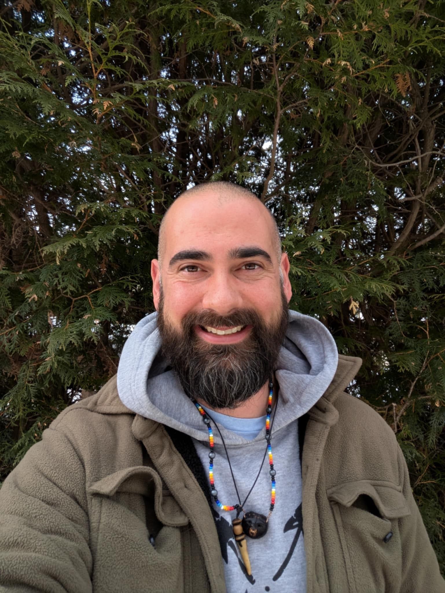 A man with a beard is smiling in front of a tree.