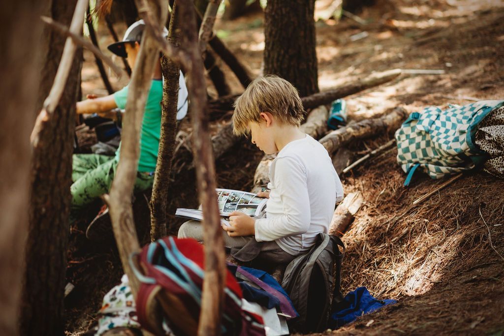 A group of children are sitting under a tree in the woods.