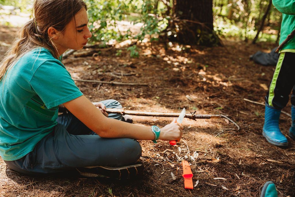 A girl is sitting on the ground in the woods making a fire.