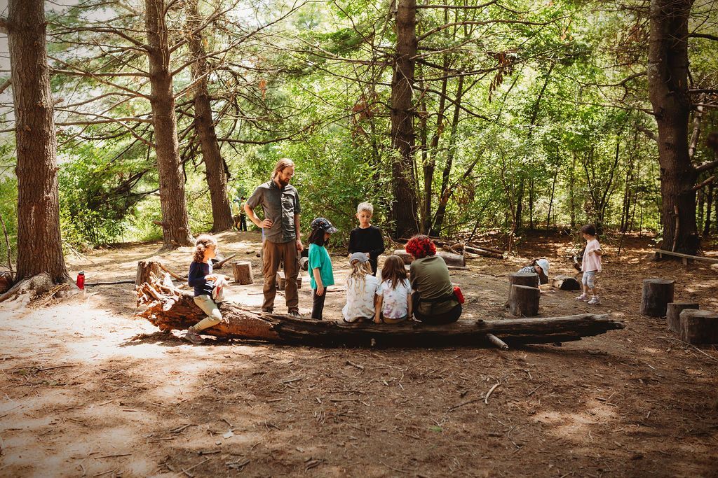 A group of people are sitting around a log in the woods.