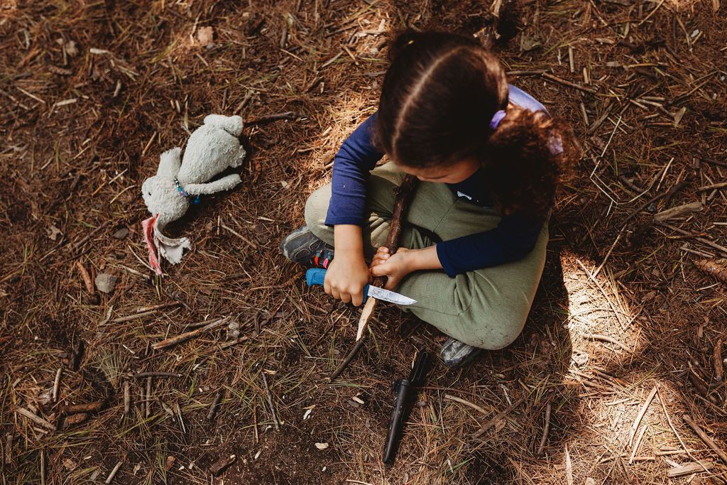 A little girl is sitting on the ground in the woods playing with a toy.