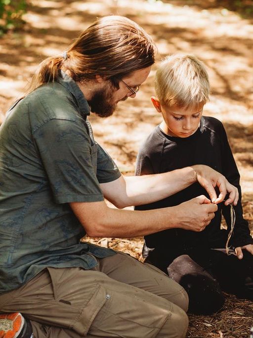 A man and a boy are sitting on the ground in the woods.