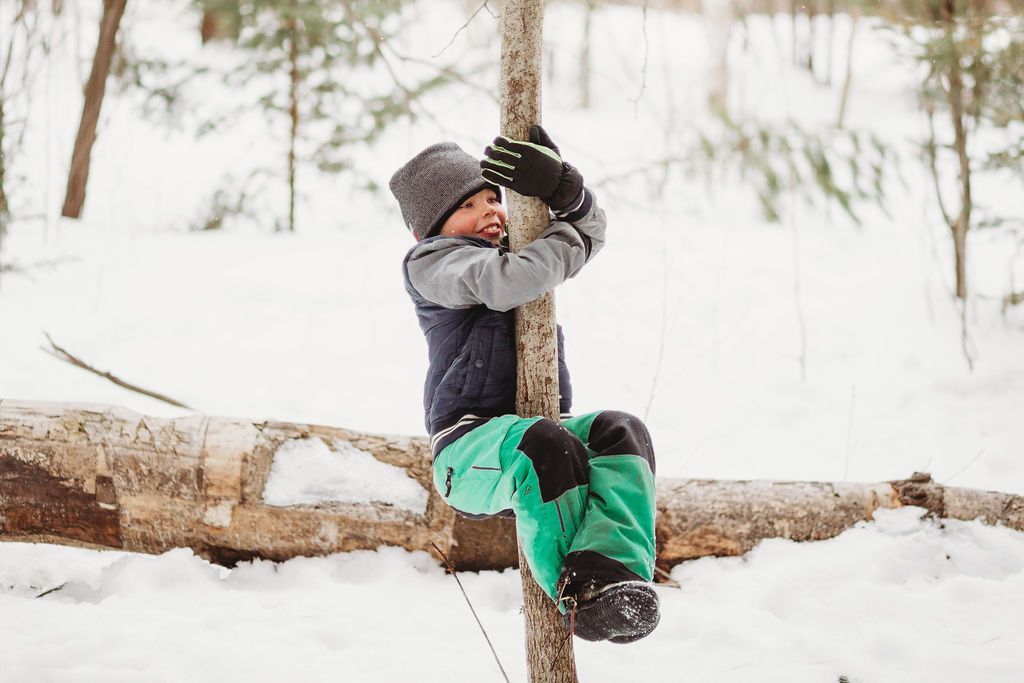 A young boy is sitting on a log in the snow.