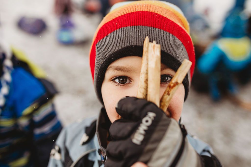 A young boy is holding a piece of wood in front of his face.