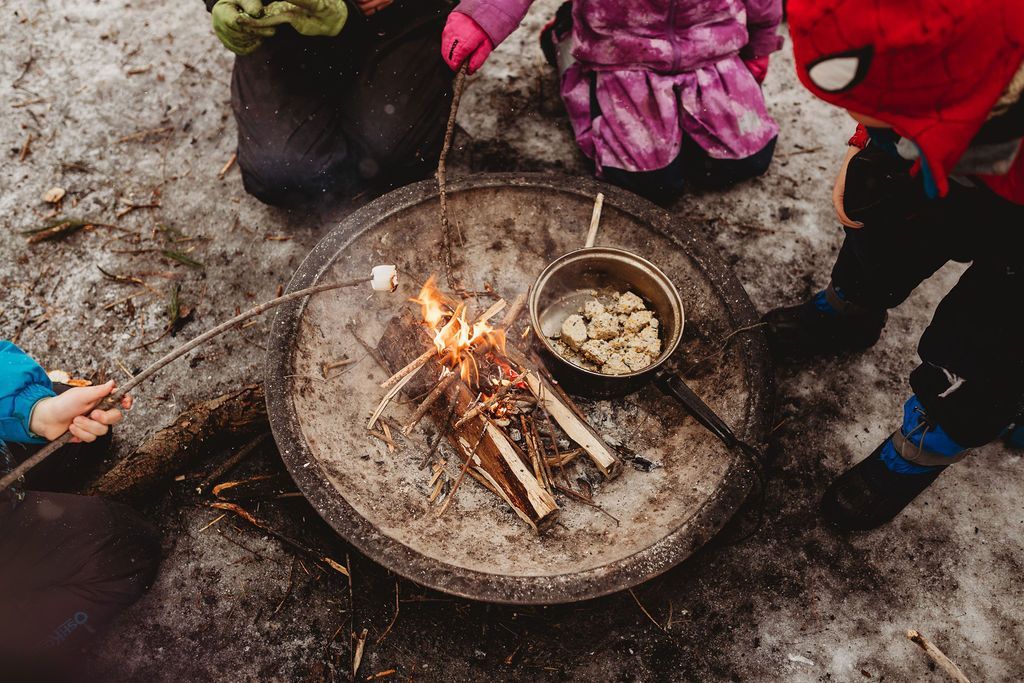A group of children are cooking food over a fire in the snow.