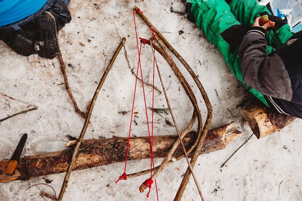 A child is laying on the ground in the snow playing with sticks.