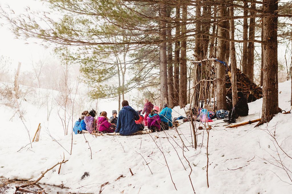 A group of children are sitting in the snow in the woods.