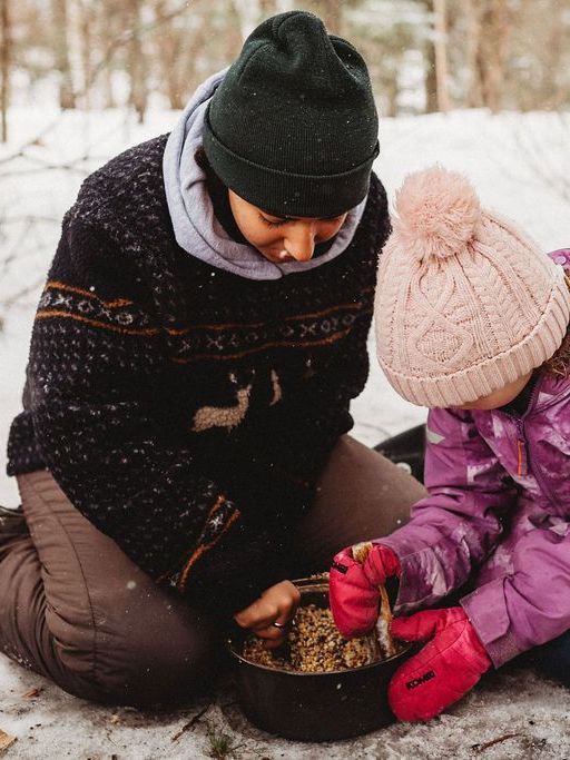 A woman and a child are kneeling in the snow cooking food in a pot.