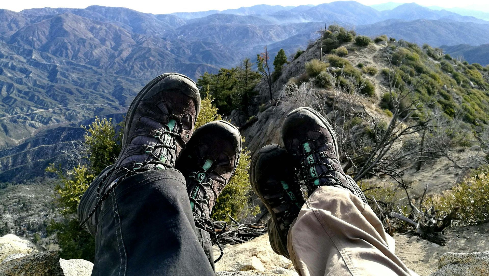 A person wearing hiking boots is sitting on top of a mountain.