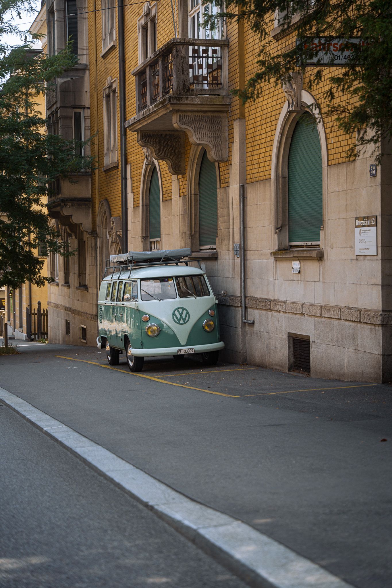 Een groen-wit busje staat geparkeerd voor een gebouw.