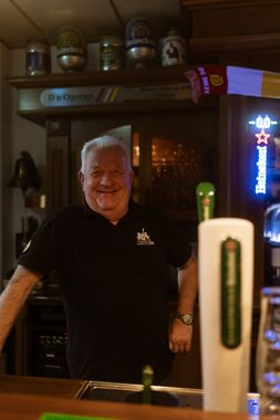 Een man in een zwart shirt staat achter een bar.