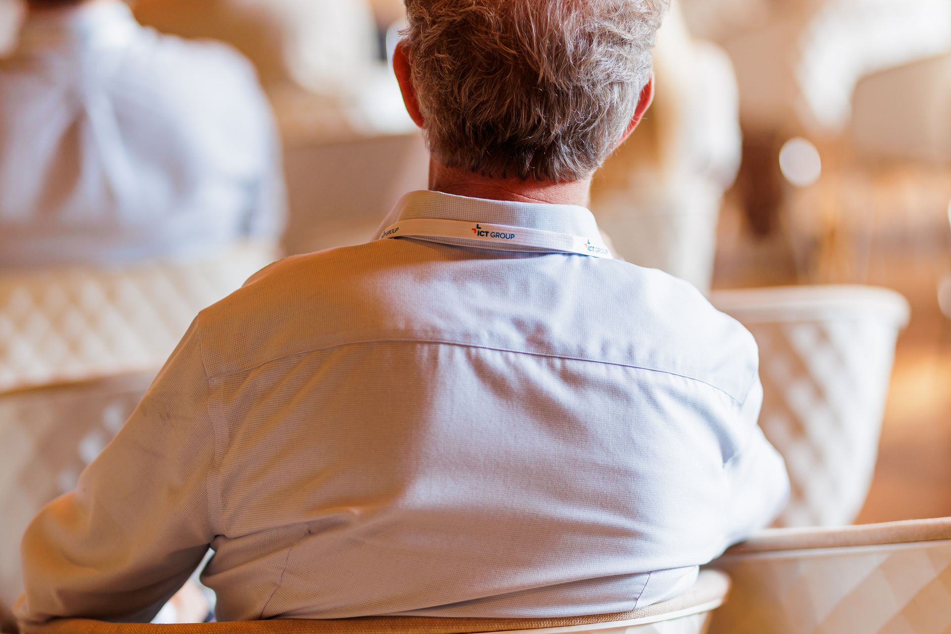 Een man zit op een stoel met zijn rug naar de camera.