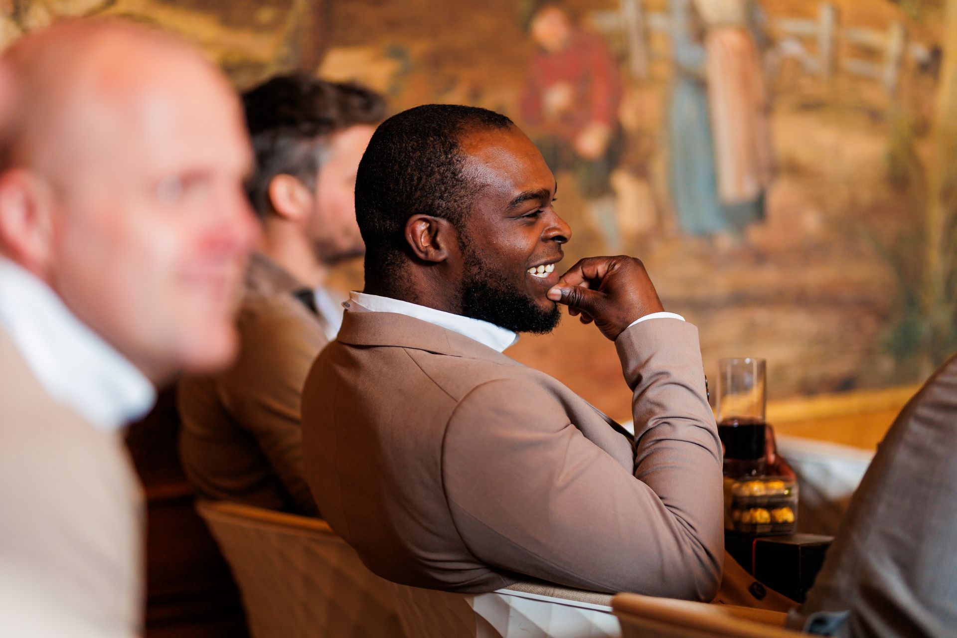 Een man in pak lacht en zit aan een tafel met andere mannen.