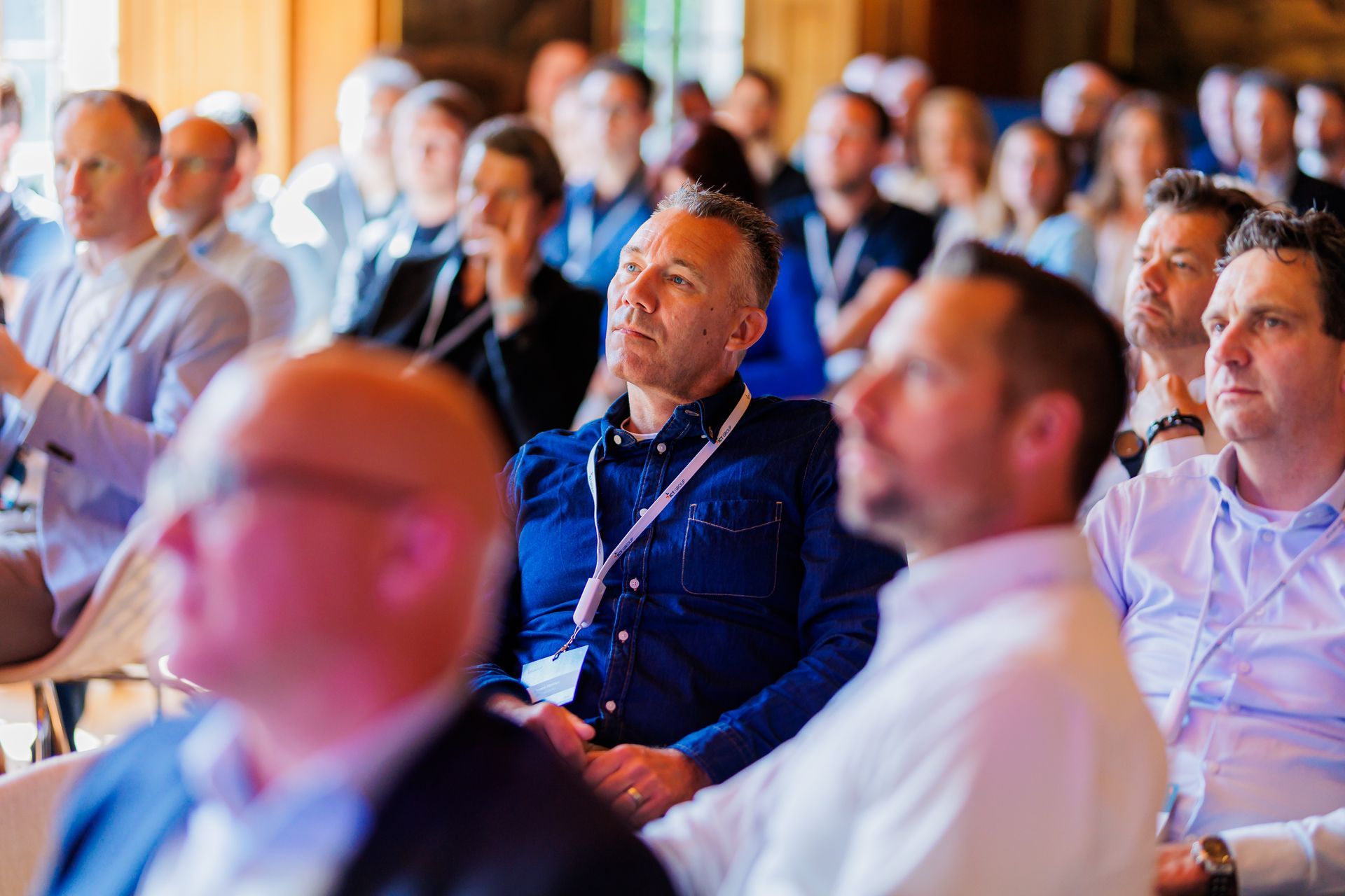Een grote groep mensen zit in een kamer en bekijkt een presentatie.