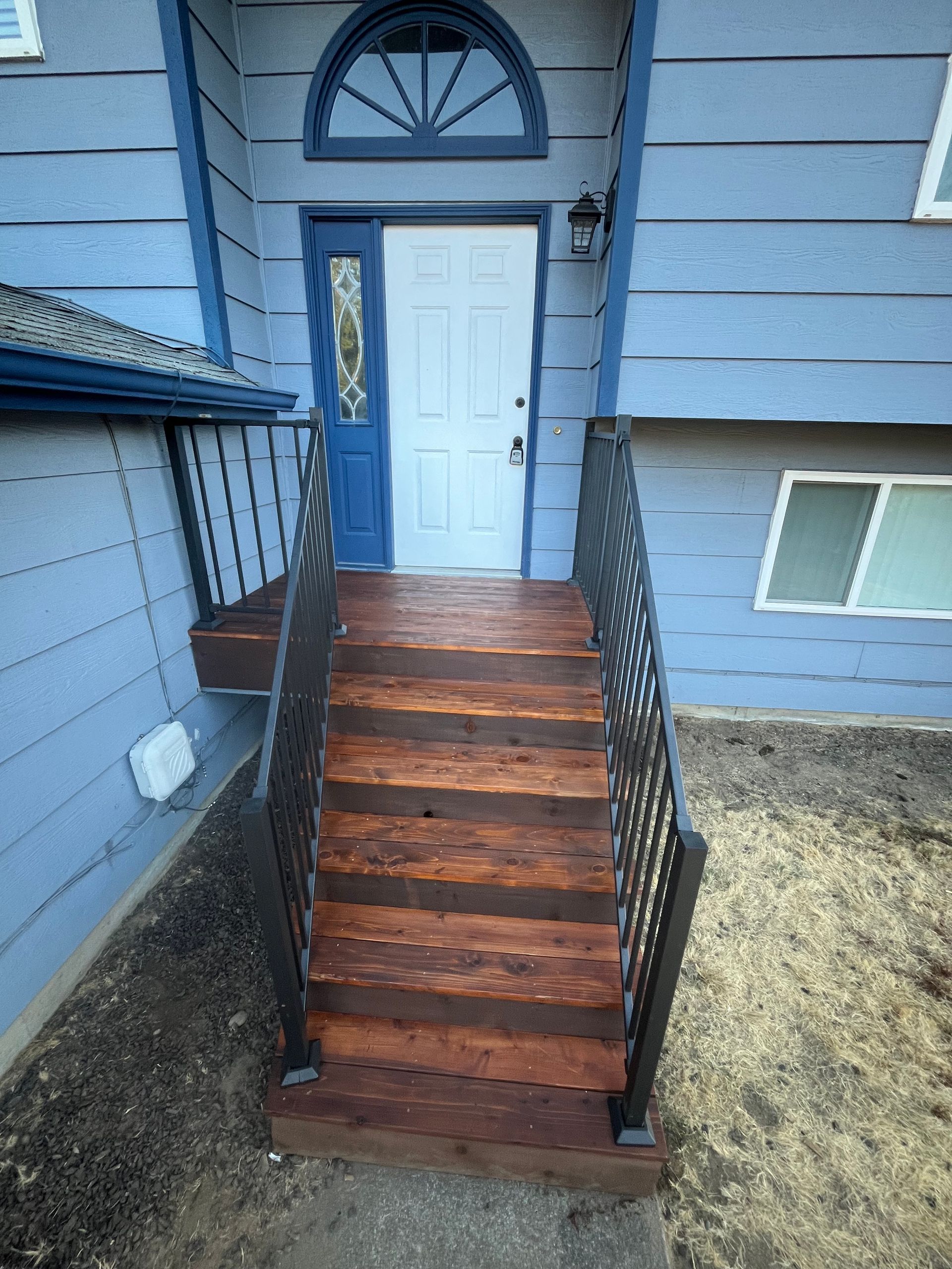 A White Deck With Black Railing and Stairs is in Front of a House