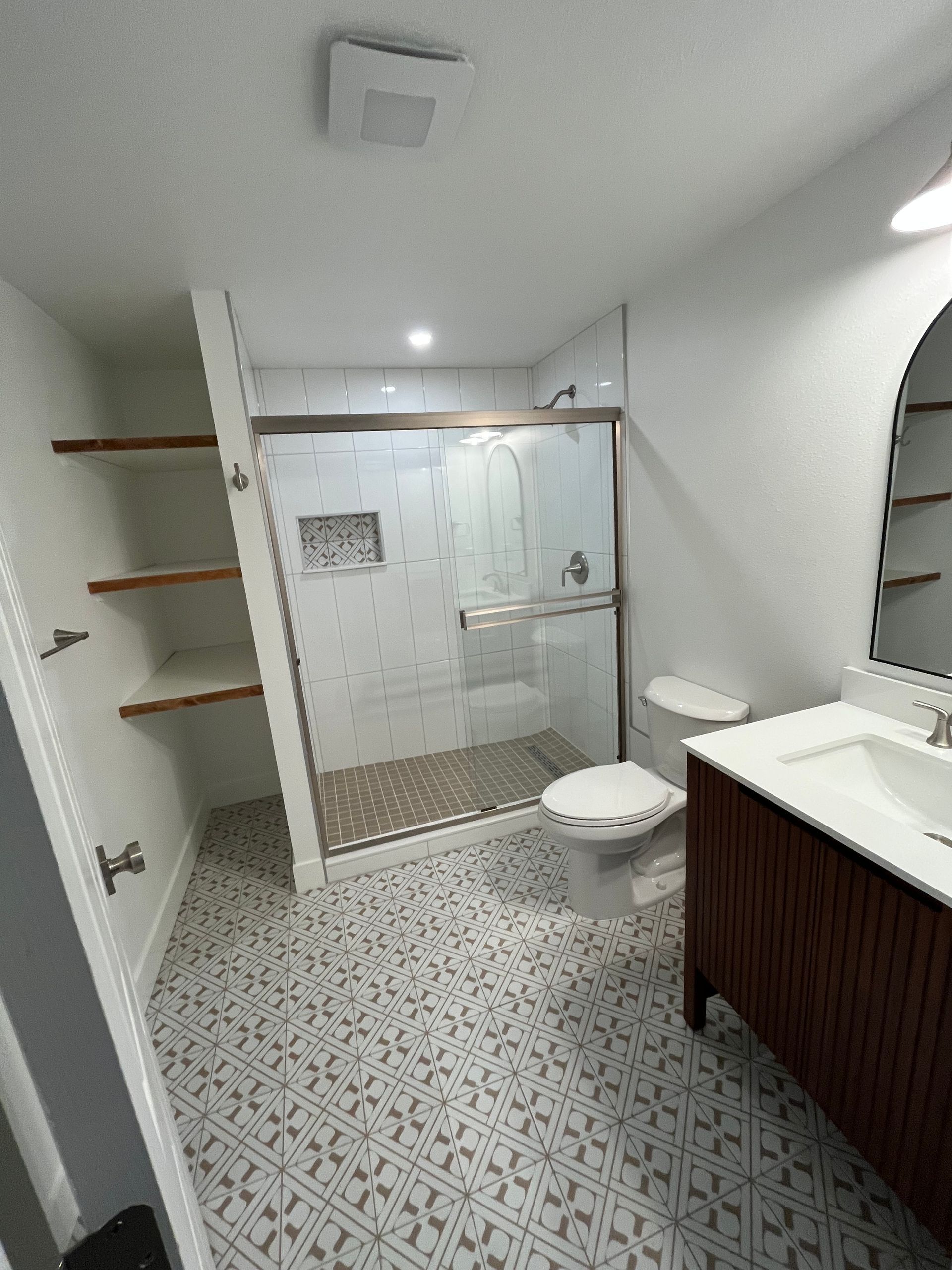 A bathroom with a toilet, sink, shower and mirror