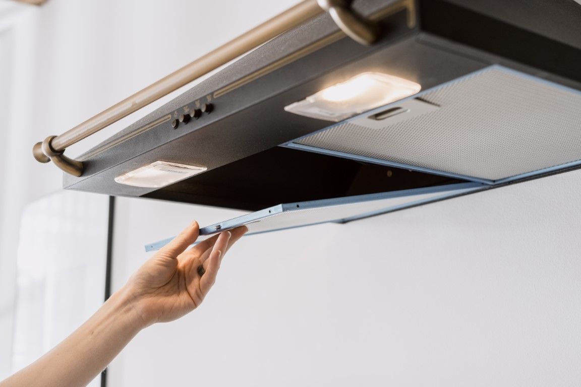Hand opening a stainless steel range hood light and vent panel