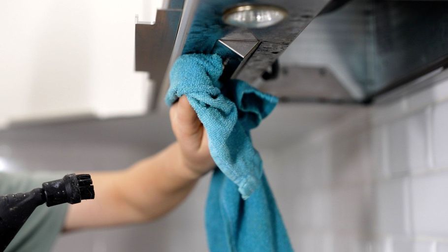 Person wiping a stainless steel kitchen hood with a blue cloth