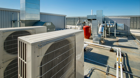Rooftop view with air conditioning units, ductwork, and pipes against a bright blue sky.
